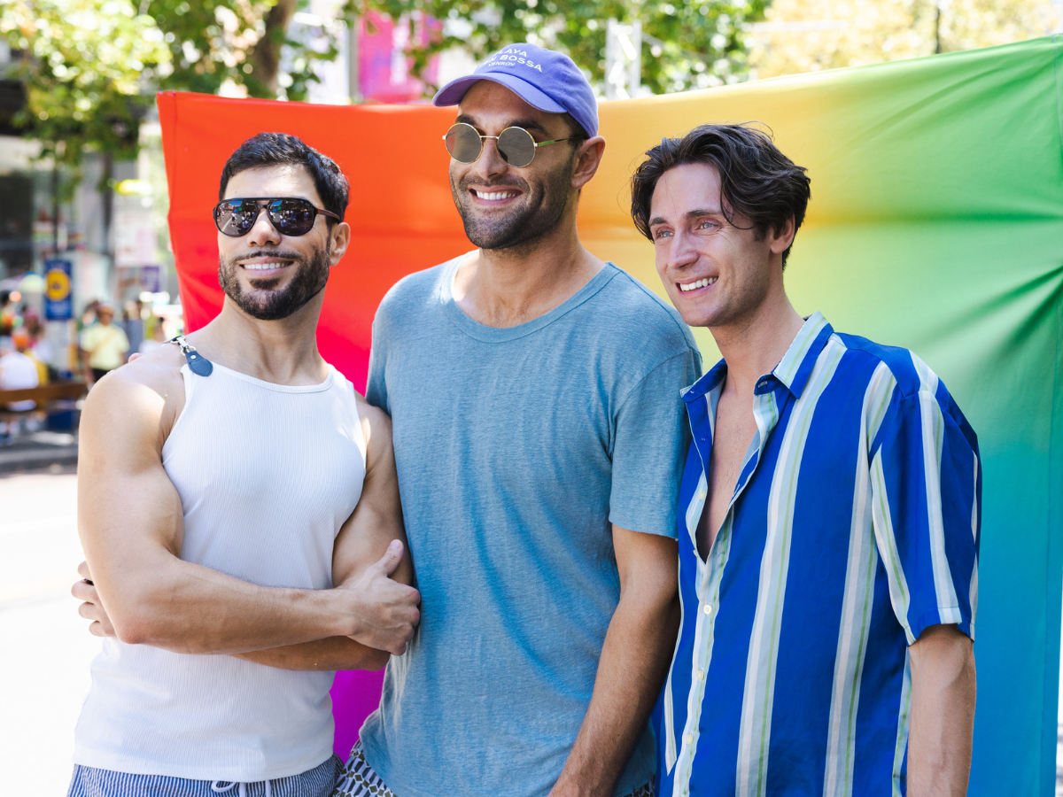 How Sperm Donation Helps Create LGBT+ Families Group of men smiling in front of a rainbow backdrop at a Pride festival in the sun